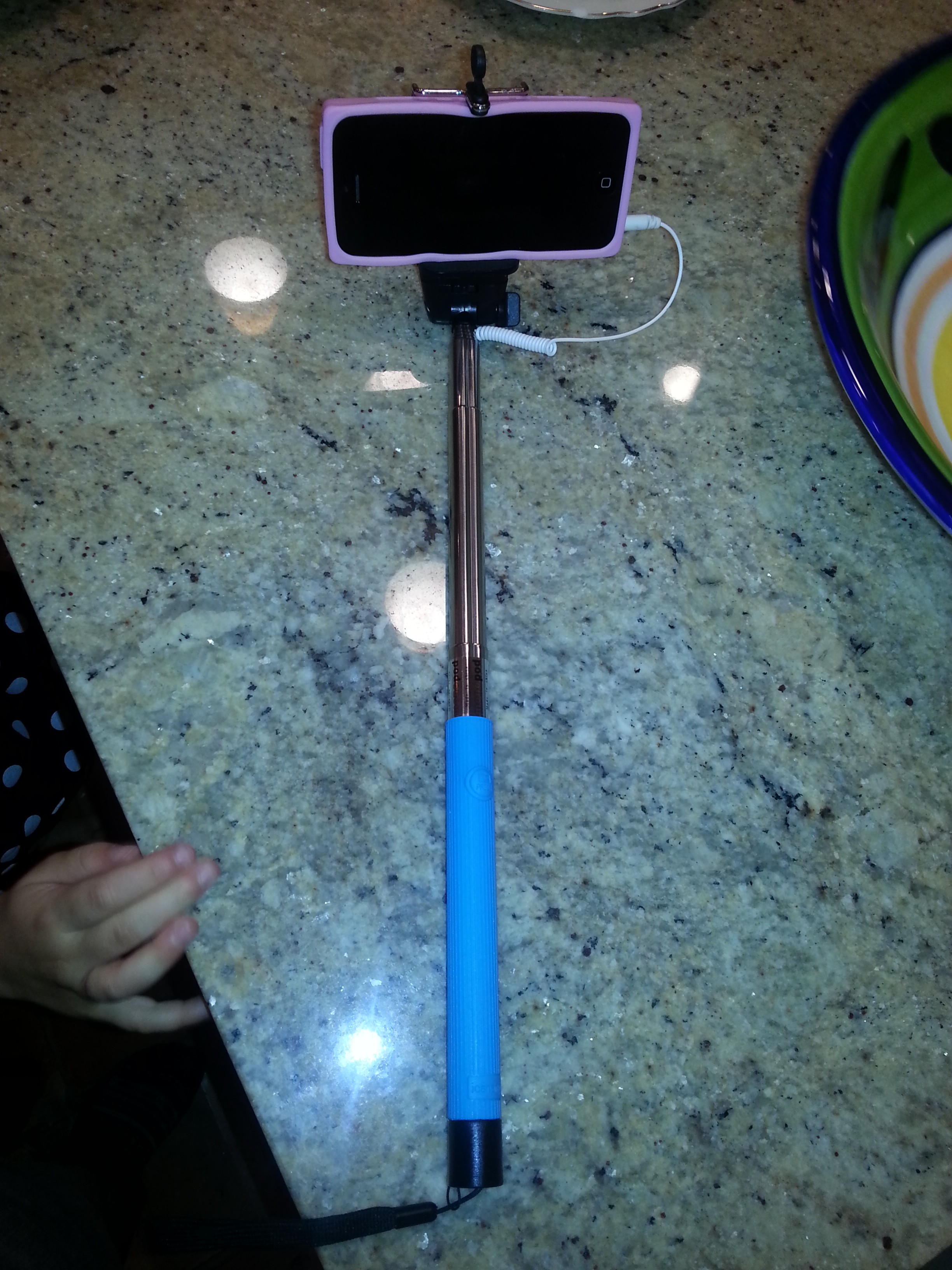 A selfie stick with an iPhone loaded into the clamp.  This selfie stick uses a headphone jack to connect the phone with the buttons on the handle. 